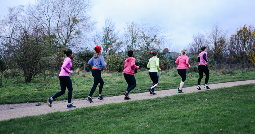 Women in athletic wear running on a path in a park.