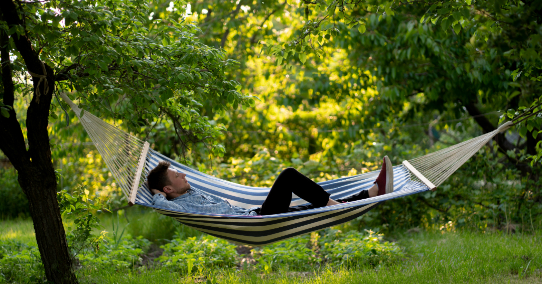 A young man relaxes outdoors, laying on a striped hammock.