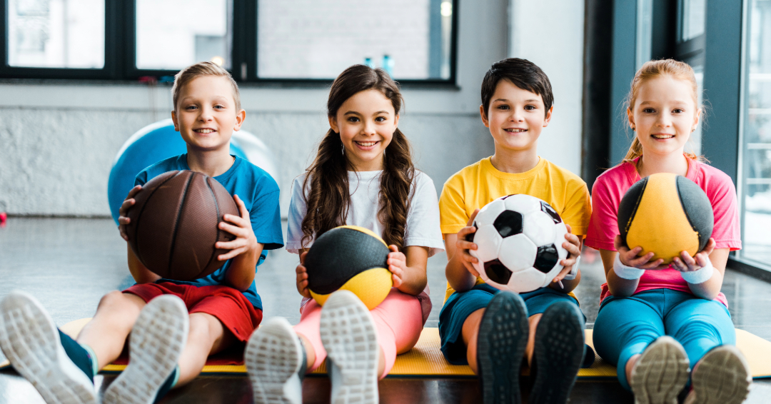 Kids at a sports camp in Franklin and Williamson Count, TN, with a football, a soccer ball, a dodgeball and a volleyball.