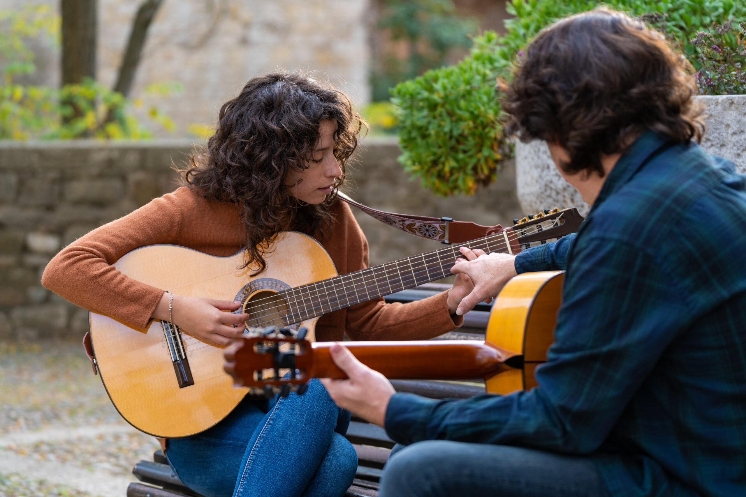 A man and a woman across from each other, playing acoustic guitars.