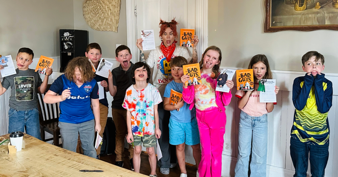 A photo of kids book club in Franklin, Tennessee, led by Anna Skates. In the photo Anna is pictured with the kids in the club, making silly faces and holding up books.