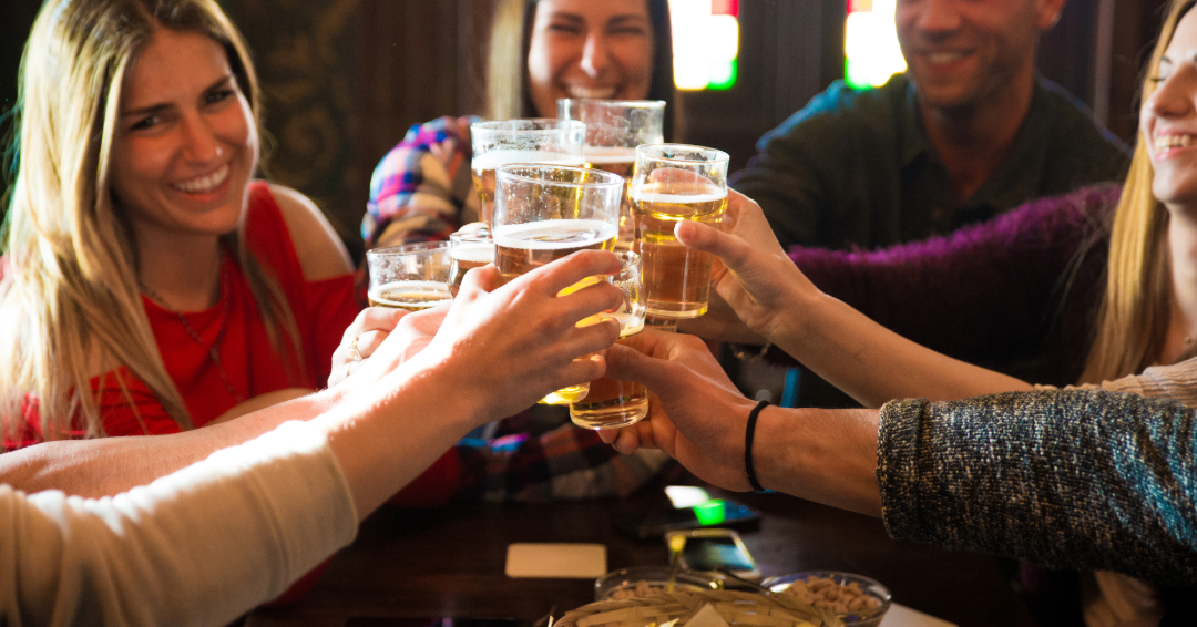 A group of lively friends are cheers-ing their drinks at a bar. 