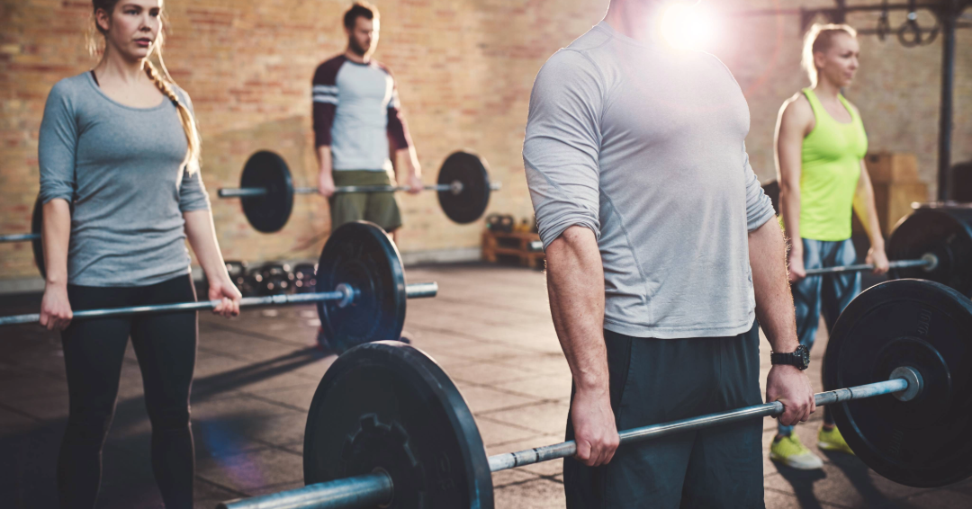 A group fitness class participates in a workout that includes deadlifting.