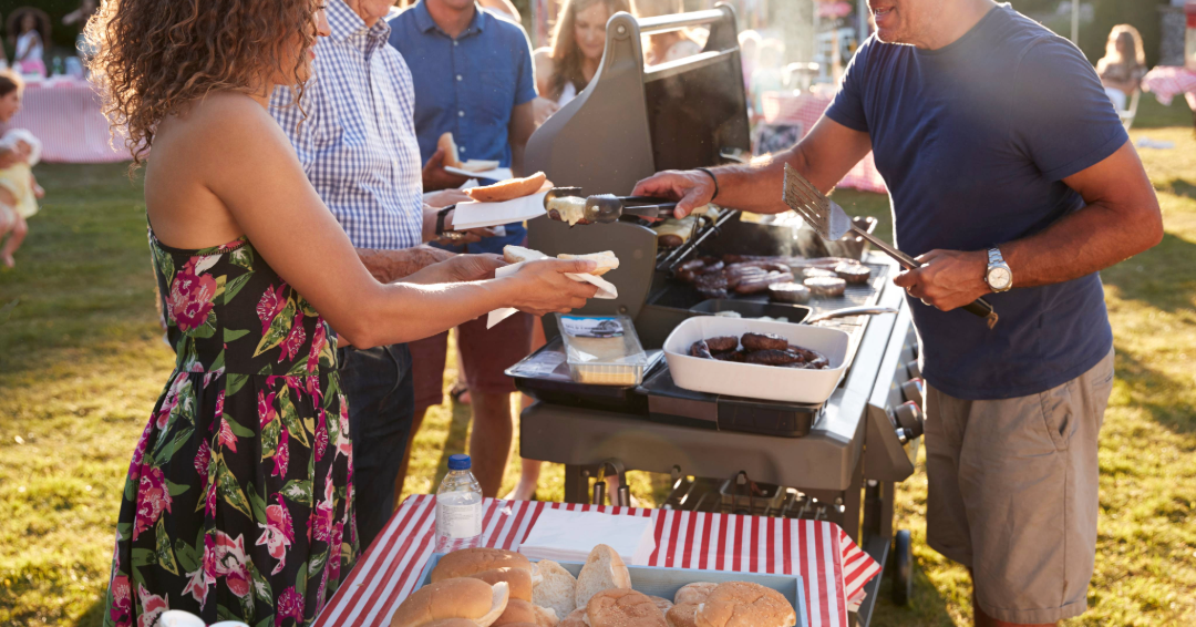 A man serves a woman barbeque at a festive, outdoor cookout. 