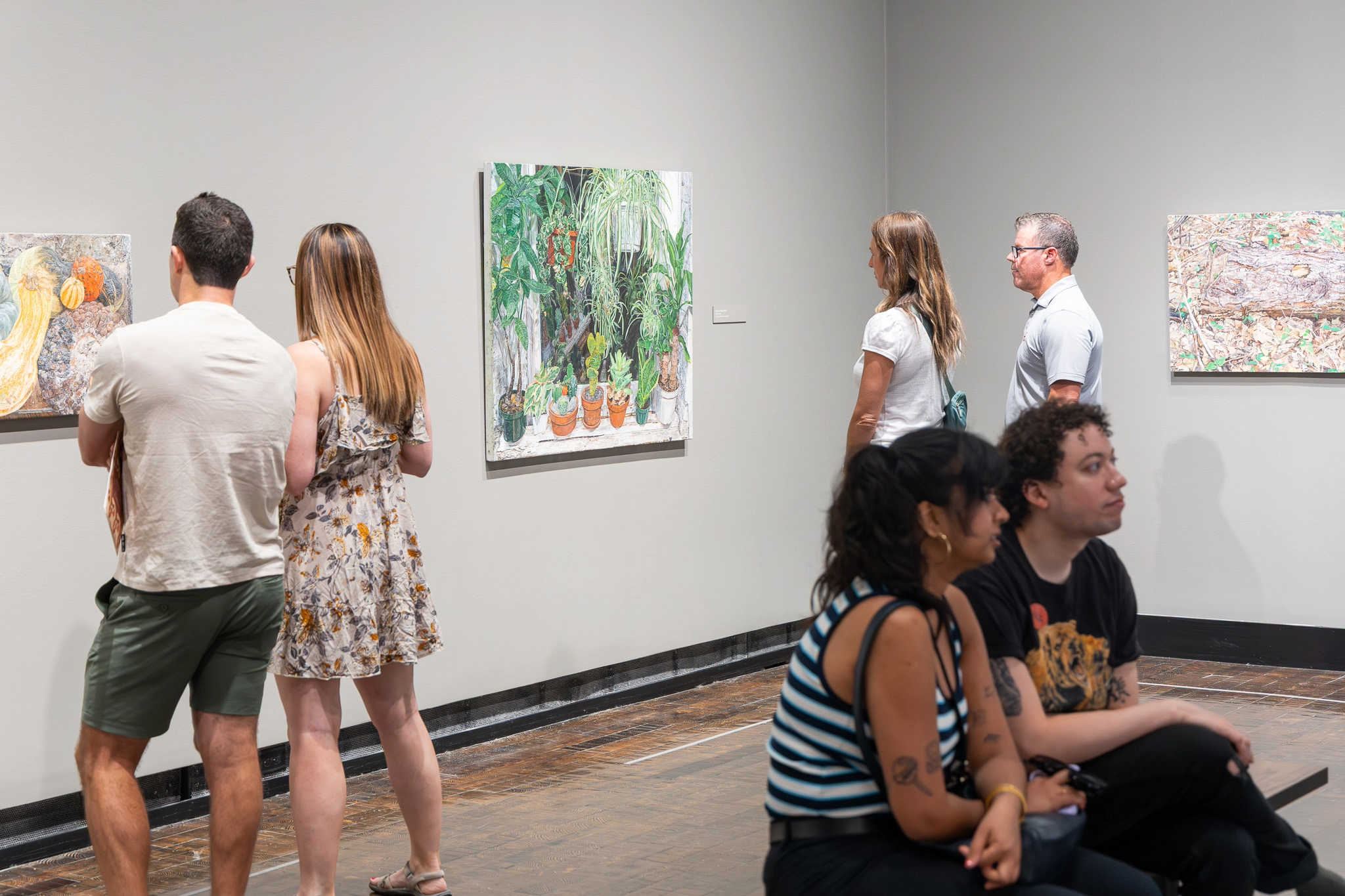 Visitors explore paintings at the Frist Art Museum in Nashville, TN, viewing detailed works that feature natural scenes and still lifes during a gallery exhibition.