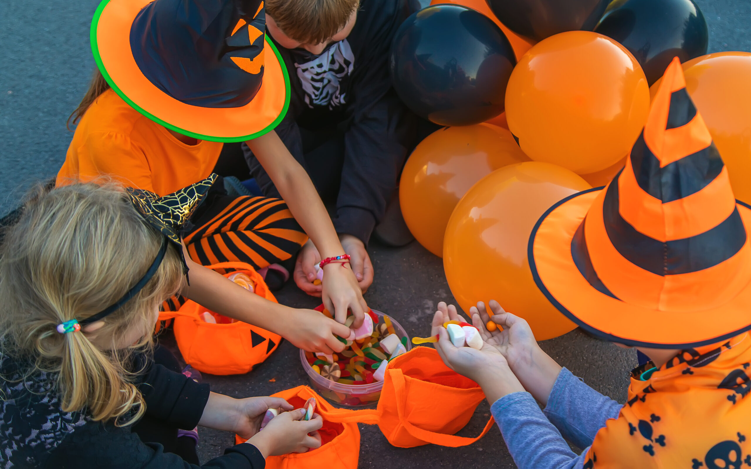 Children in Halloween costumes sitting on the ground sorting through candy near orange and black balloons during a community trunk-or-treat event in Franklin, Tennessee.
