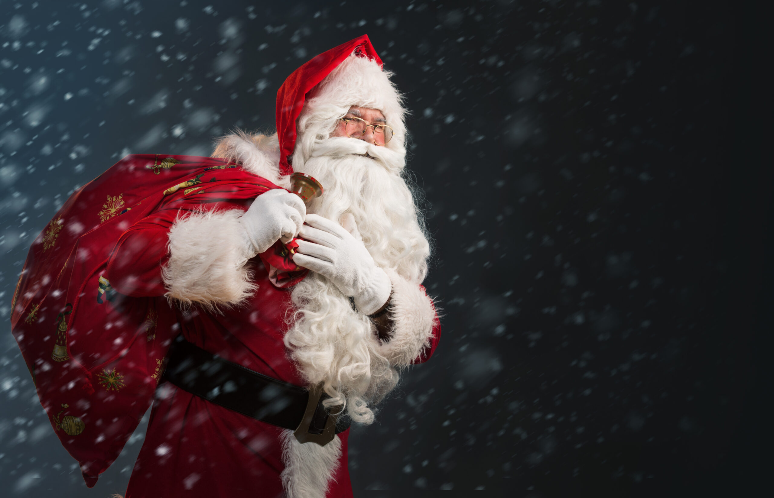 Santa Claus holding a bag with presents and ringing a bell on a dark background with snow